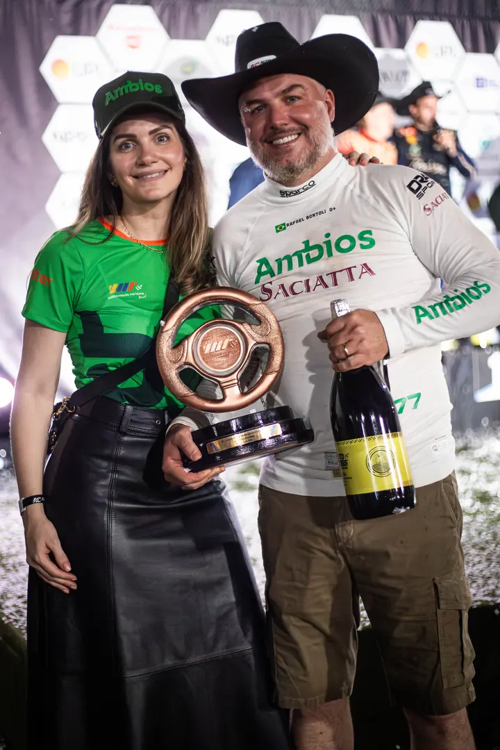 Rafael de chapéu com troféu e espumante ao lado de uma mulher de camiseta verde
